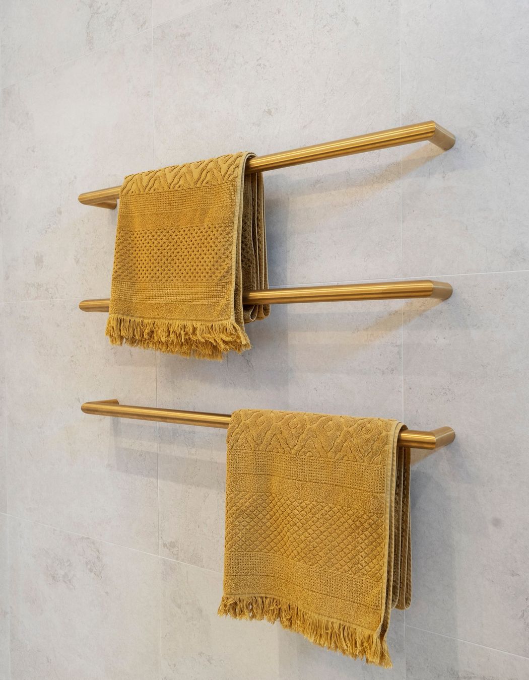 The individual brushed brass heated towel rails are a strikingly elegant yet minimalist addition to the bathroom, perfectly contrasting against the Breccia white matt wall tiles. Their sleek design not only enhances the aesthetic appeal of the space but also provides practical warmth and comfort. The warmth of the brass against the crisp white tiles creates a sophisticated interplay of color and texture, elevating the overall elegance of the bathroom while ensuring functionality and style.