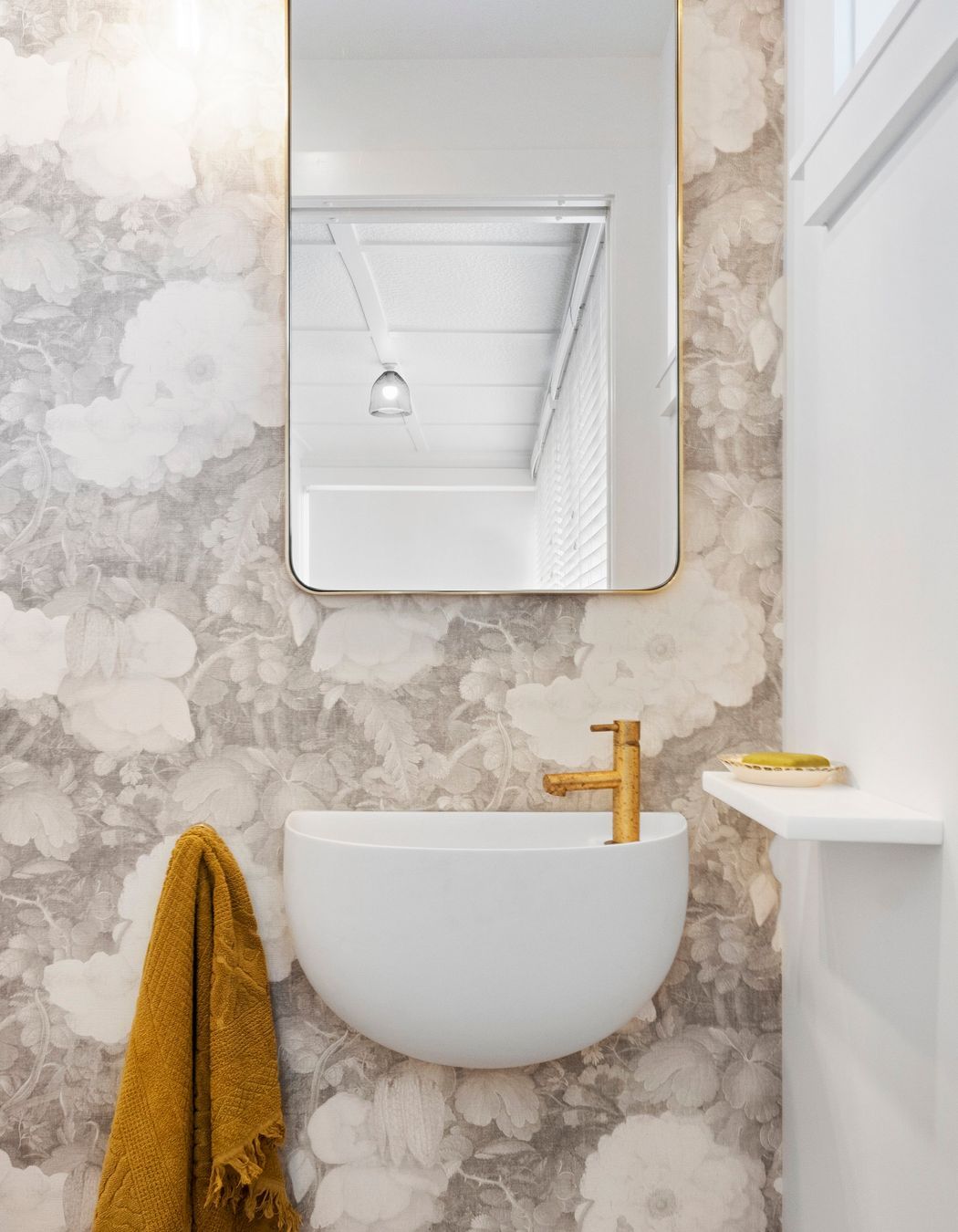 The stunning curved wall-hung Lavamani round basin harmoniously complements the custom linen wallpaper, creating a seamless blend of elegance and artistry. Its graceful shape adds visual interest and softens the overall aesthetic, while the intricate floral patterns of the wallpaper enhance the basin's refined design. Together, they create a beautifully curated focal point in the powder room, infusing the space with a sense of style and tranquility.