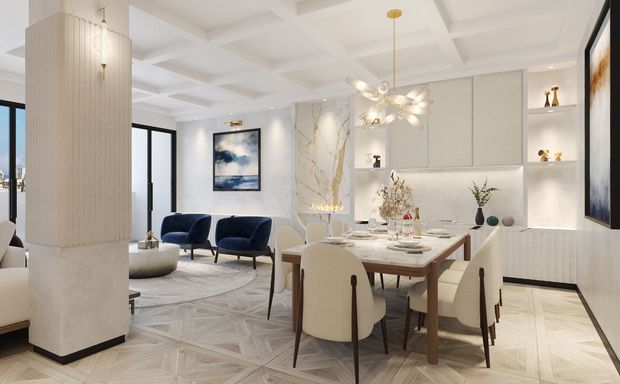 Bright open-plan dining and living area with a refined contemporary interior. A sculptural dining table with upholstered cream chairs occupies the foreground, while a pair of deep blue lounge chairs sits beyond. The room features a white coffered ceiling, fluted wall column, pale geometric timber flooring, integrated illuminated shelving and cabinetry, marble-look feature surfaces, black-framed glazing, and a statement pendant light.