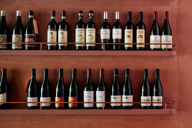 Close-up of two long wooden display shelves mounted against a warm terracotta plaster wall, densely lined with upright wine bottles. The built-in shelving and coordinated earthy palette create a refined wine-storage display.