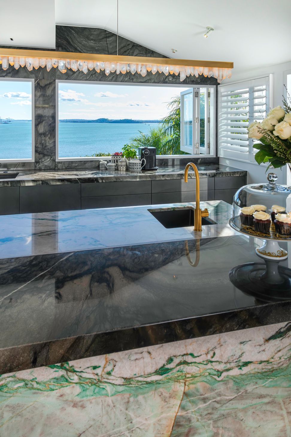 A daytime drinks area is centered around a brass-rendered tap dispensing chilled, sparkling and boiling water on the island. Related coffee cups, teas boxes and glasses are stored in touch-motion drawers opposite. Several custom-dimensioned drawers hosting the owners’ extensive dinnerware and serveware collections, are positioned conveniently beside the dishwasher.