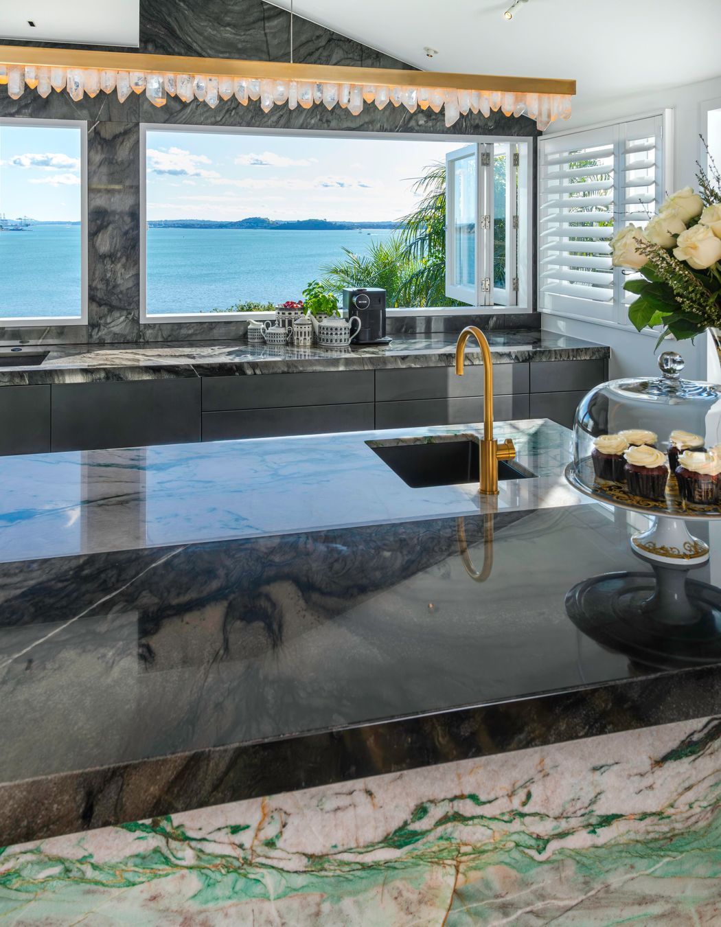 A daytime drinks area is centered around a brass-rendered tap dispensing chilled, sparkling and boiling water on the island. Related coffee cups, teas boxes and glasses are stored in touch-motion drawers opposite.  Several custom-dimensioned drawers hosting the owners’ extensive dinnerware and serveware collections, are positioned conveniently beside the dishwasher.