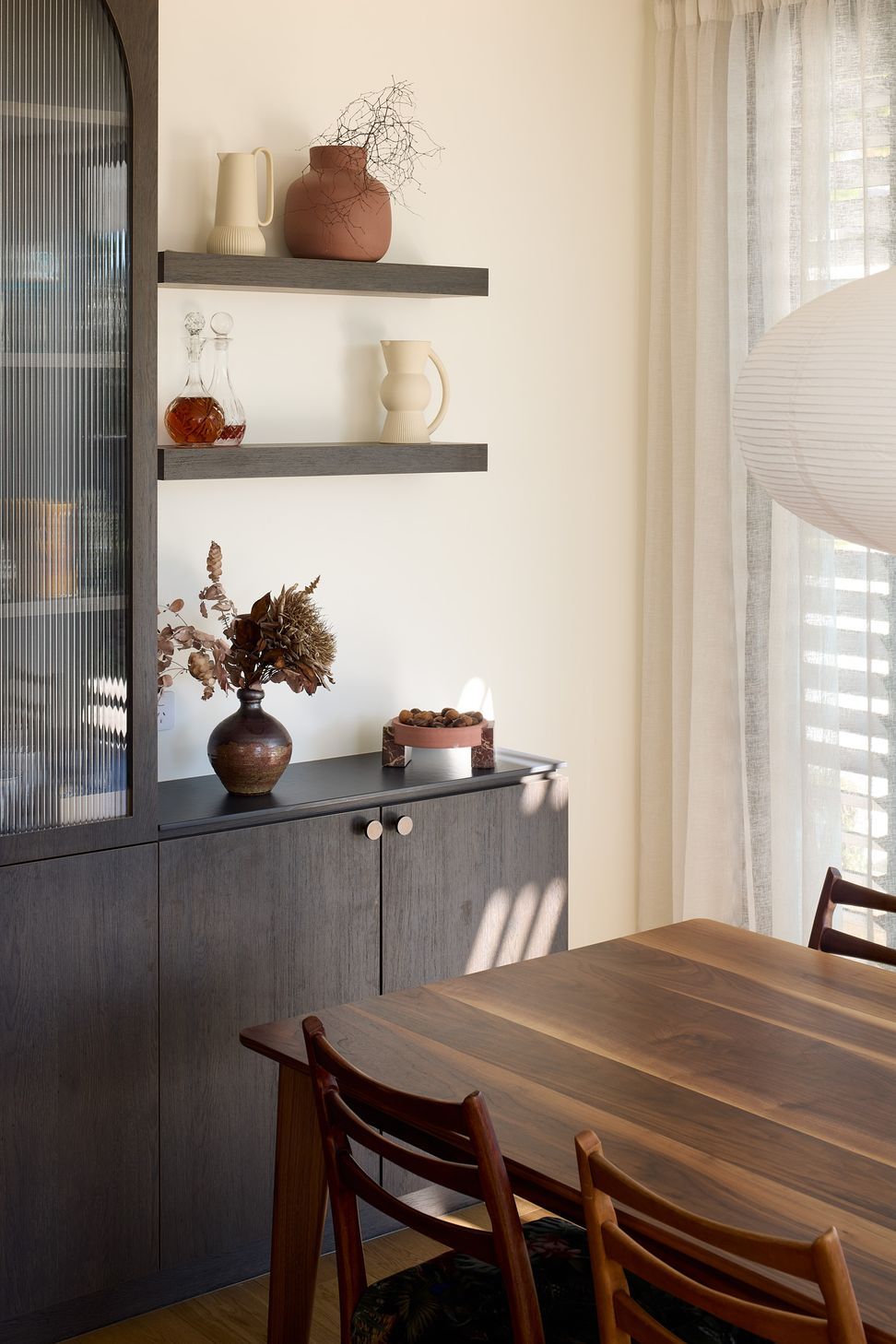The dining area is framed by bespoke dark oak cabinetry, including a tall fluted glass display cabinet that introduces texture and craftsmanship while providing elegant storage.
