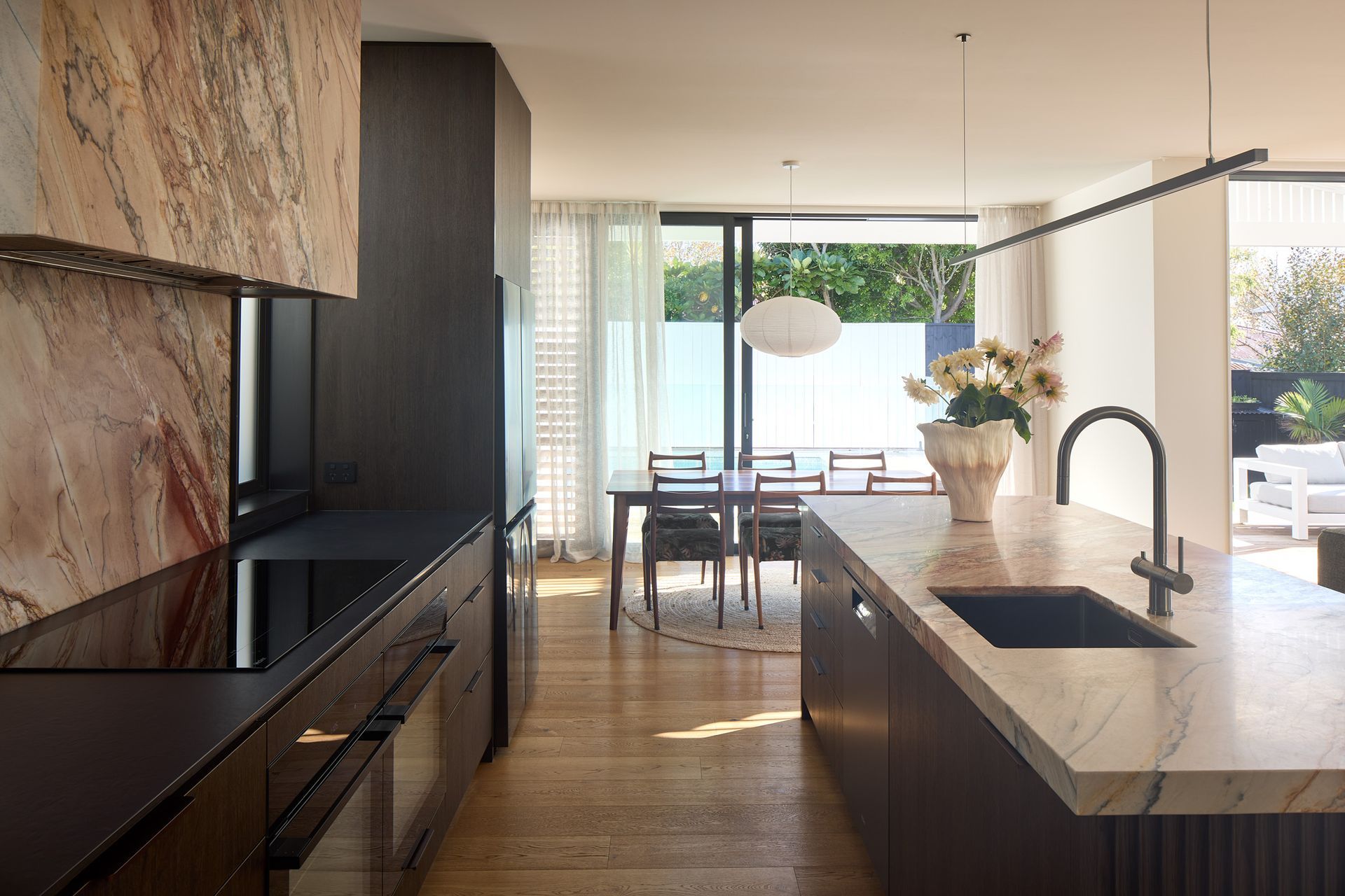 From the kitchen, views extend through the dining room to the garden and swimming pool beyond. Large openings strengthen the connection between the interior and the landscaped outdoor living spaces.