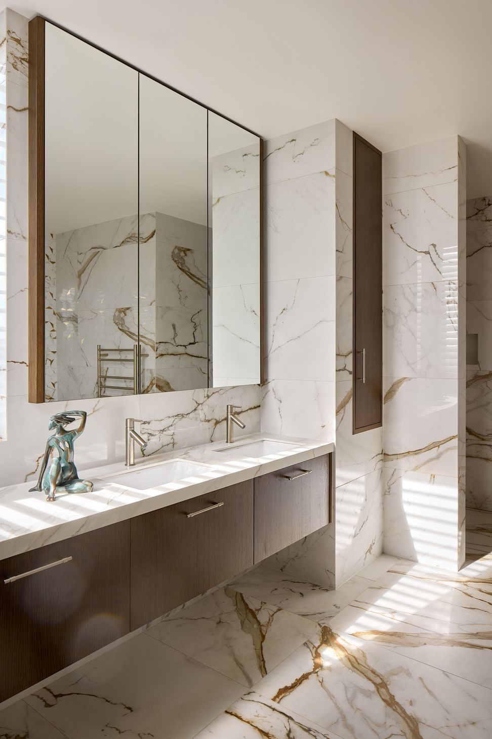 The bespoke vanity combines dark timber cabinetry, a stone benchtop and a custom mirror within the richly textured ensuite. The integrated laundry chute is carefully incorporated into the joinery for a seamless finish.