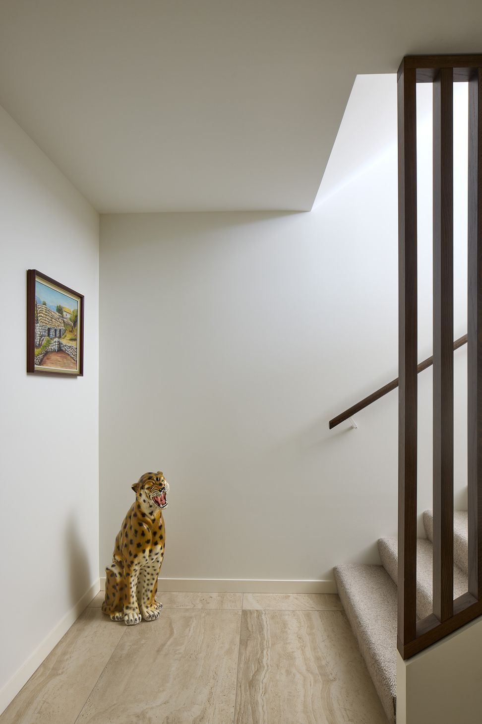 At the base of the staircase, a full-height timber screen brings warmth and rhythm to the entrance hall. Tiled flooring and a sculptural ceramic leopard add texture, character and a playful moment within the refined interior.