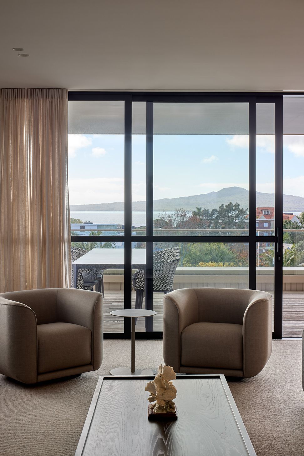 From the living room, expansive glazing frames the covered deck and sweeping views across the Hauraki Gulf. The elevated outlook brings light, landscape and the changing coastal environment into the heart of the home.