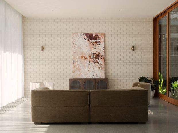 A bright, refined living room viewed from behind a large brown sofa. The room features a pale painted brick feature wall, light timber or concrete-look flooring, sheer full-height curtains, a low dark timber sideboard, abstract artwork, wall sconces, and warm timber-framed glazing or doors along the right side. Indoor plants add natural texture.