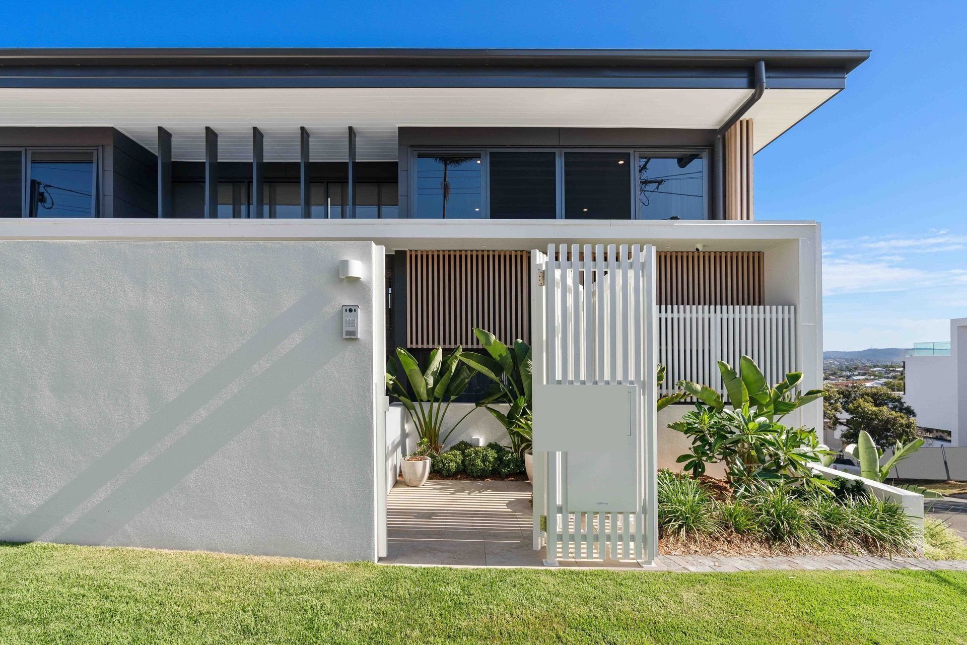 White timber battens frame the entry, the home stepping down the hillside toward the city.
