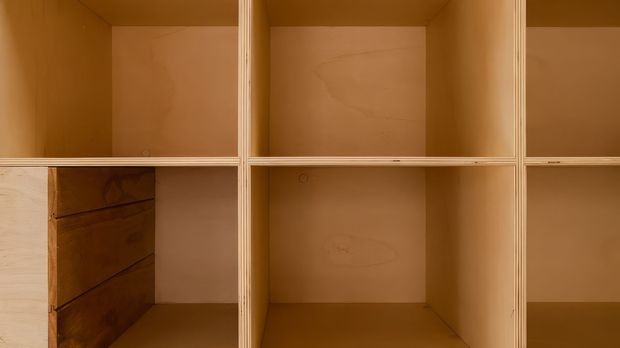 Close-up of built-in open shelving or storage cabinetry made from warm-toned plywood, with multiple square compartments, visible layered plywood edges, and a few lower drawers. The image focuses on the joinery and wood grain; no room context is visible.
