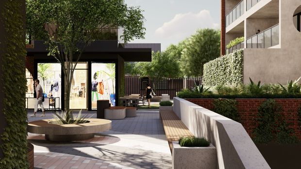 A landscaped urban courtyard or pedestrian terrace between contemporary buildings. The scene features paved walkways, raised planters, built-in curved concrete seating around a mature tree, timber bench seating, dense hedging, brick retaining walls, and a dark-framed glazed retail or lobby pavilion. A multi-storey contemporary building with balconies is visible on the right.
