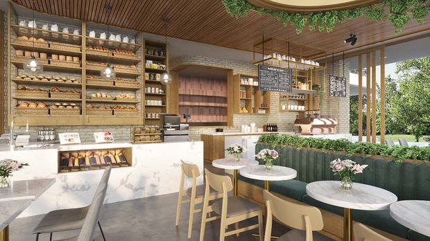 A bright, upscale café interior with a bakery display and service counter, open shelving filled with bread and pastries, a coffee and drinks station, and a dining area furnished with small round marble-top tables, light timber chairs, and a curved green upholstered banquette. Warm timber slatted ceilings, timber shelving, indoor greenery, floral arrangements, and large glazed openings create an inviting connection to the outdoors.