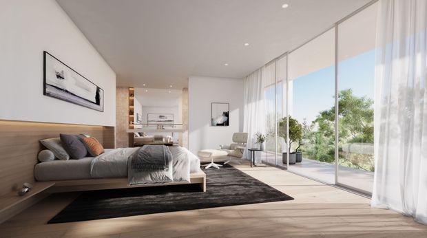 Bright contemporary bedroom with a low platform bed set against a warm timber feature wall, neutral bedding and cushions, a dark area rug, minimalist artwork, and a small lounge chair. Full-height glazed sliding doors with sheer curtains open to a leafy outdoor setting, creating an airy indoor-outdoor connection.
