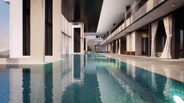 A long indoor swimming pool runs through a highly modern, resort-like architectural space. The pool is bordered by pale stone or concrete surfaces, with tall floor-to-ceiling glazing, dark vertical frames, dramatic black ceiling planes, recessed lighting, and an upper-level gallery or balcony. Draped curtains and reflective water create a luxurious, serene atmosphere.