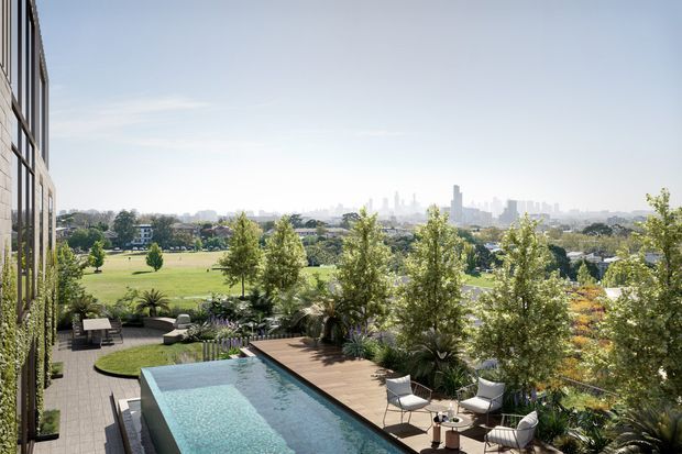 Elevated exterior view from a modern multi-storey building, looking over a landscaped terrace with a rectangular swimming pool, timber deck, outdoor lounge furniture, and lush planting. A broad green park and distant urban skyline are visible beyond the property.