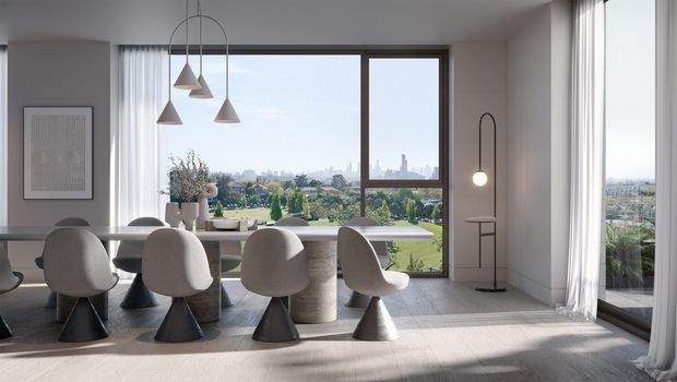 A bright contemporary dining room with a long dining table and sculptural upholstered chairs arranged beside expansive floor-to-ceiling windows. Neutral grey and off-white finishes, sheer curtains, pendant lights, and a slender floor lamp create a refined, airy interior, with a leafy urban landscape visible beyond the glazing.