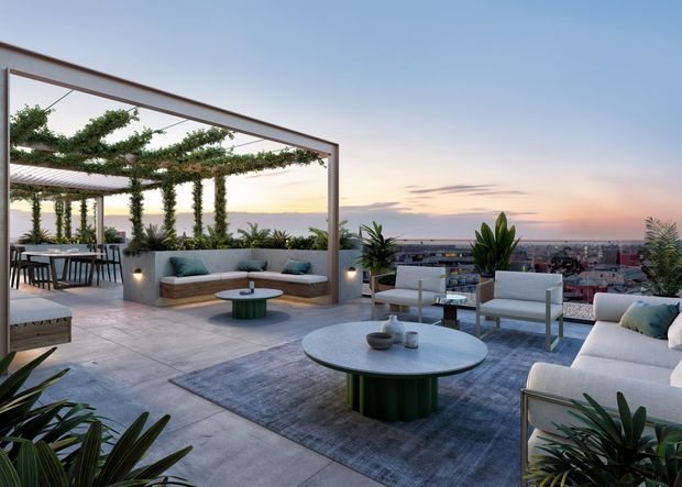 A spacious rooftop terrace overlooking a city at sunset, arranged as an outdoor living and dining area. The terrace features a large open pergola with climbing greenery, built-in concrete seating with teal cushions, freestanding sofas and lounge chairs, a round coffee table, dining furniture, tiled or concrete paving, and abundant potted plants. The overall design is contemporary, relaxed, and resort-like, with expansive urban views.