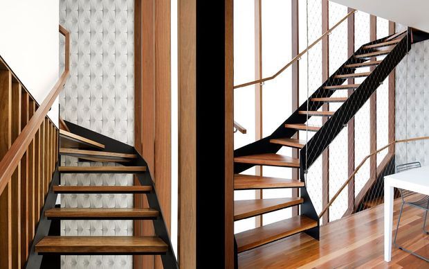 Interior architectural photograph focused on a contemporary staircase with dark metal stringers and open timber treads. The stair is set against a distinctive tufted geometric wall panel, with vertical timber wall elements, slim timber handrails, black cable balustrading, and polished timber flooring. A small portion of a white desk is visible at right.