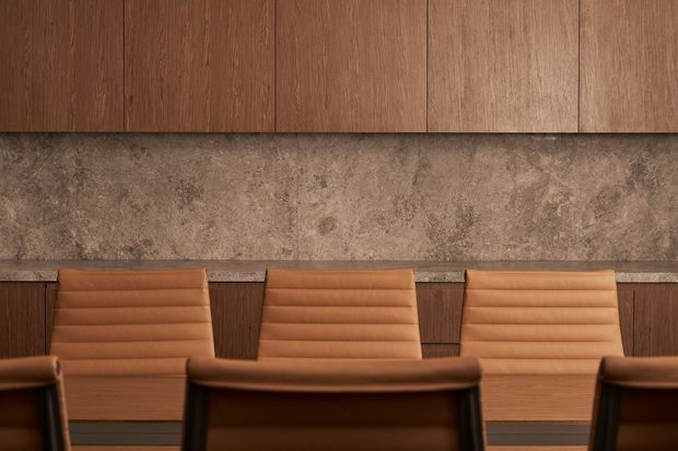 Close-up interior view of a warm, refined dining or meeting area featuring a long timber-clad wall, a textured stone-look feature wall, and tan leather upholstered chairs around a dark wood table.