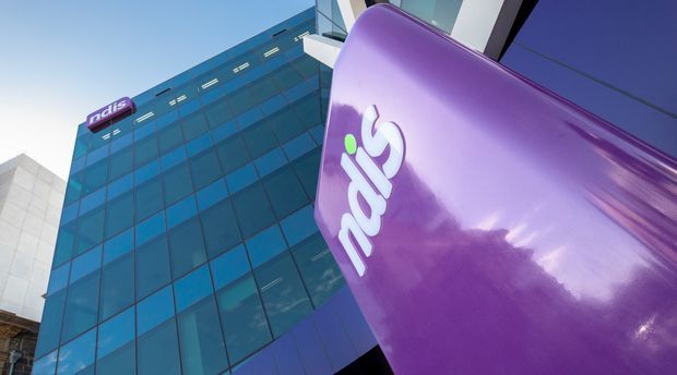 Low-angle exterior view of a contemporary multi-storey commercial building with a blue reflective glazed curtain wall and prominent purple retail signage in the foreground. The composition emphasizes the building facade and corporate branding against a clear sky.