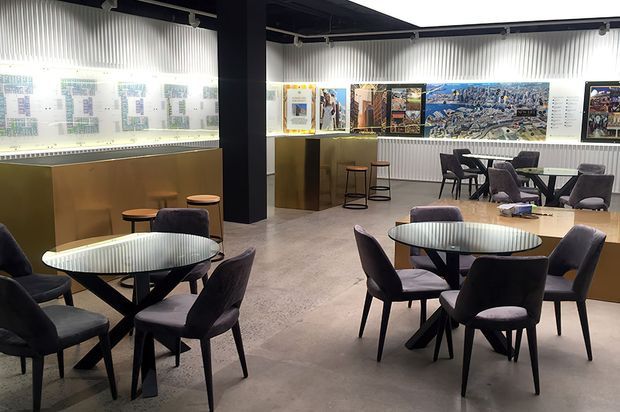 A contemporary exhibition or gallery-style commercial interior with several round dining tables and upholstered chairs arranged across a polished concrete floor. Black structural columns, dark ceilings, illuminated display walls, framed artwork, and timber-toned cabinetry create a refined hospitality and showroom atmosphere.