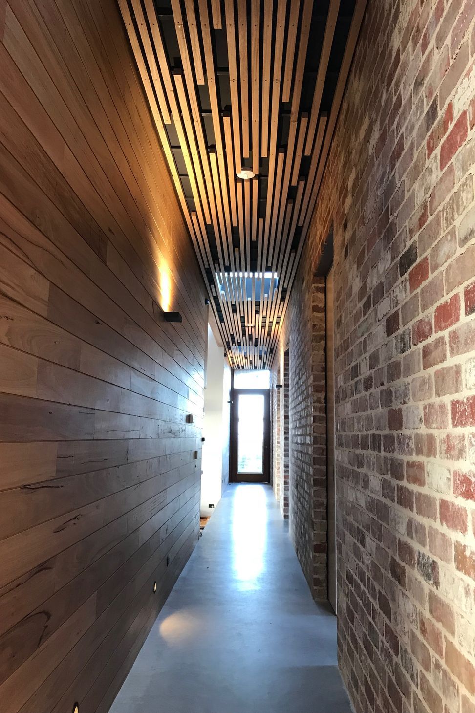 A linear Breezway space connecting to the kitchen garden features natural timber batten ceiling, recycled brick and board walls