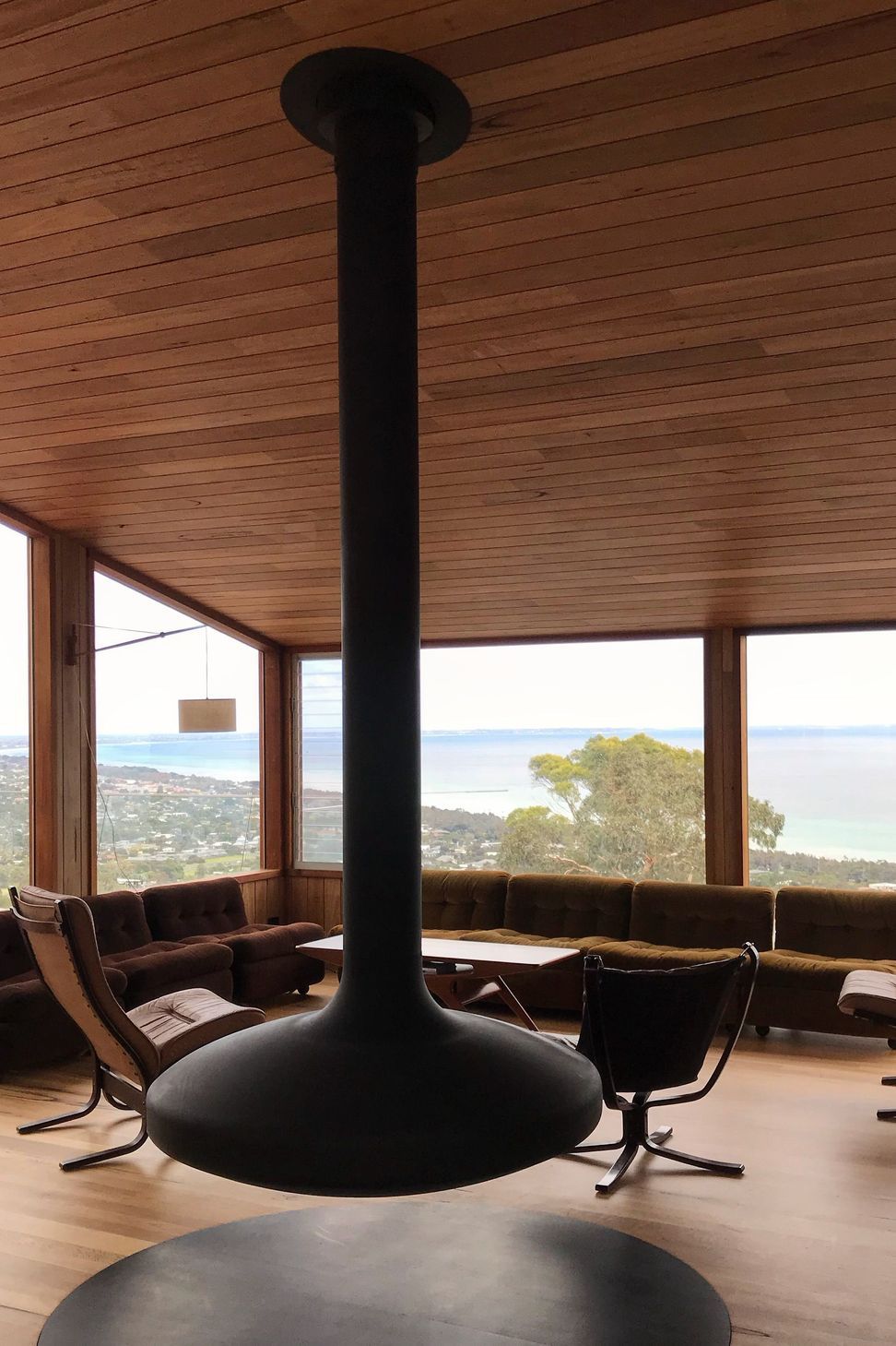 The Oblica suspended fireplace provides a sculptural focal point, anchored by continuous timber-lined ceilings and a vast coastal panorama
