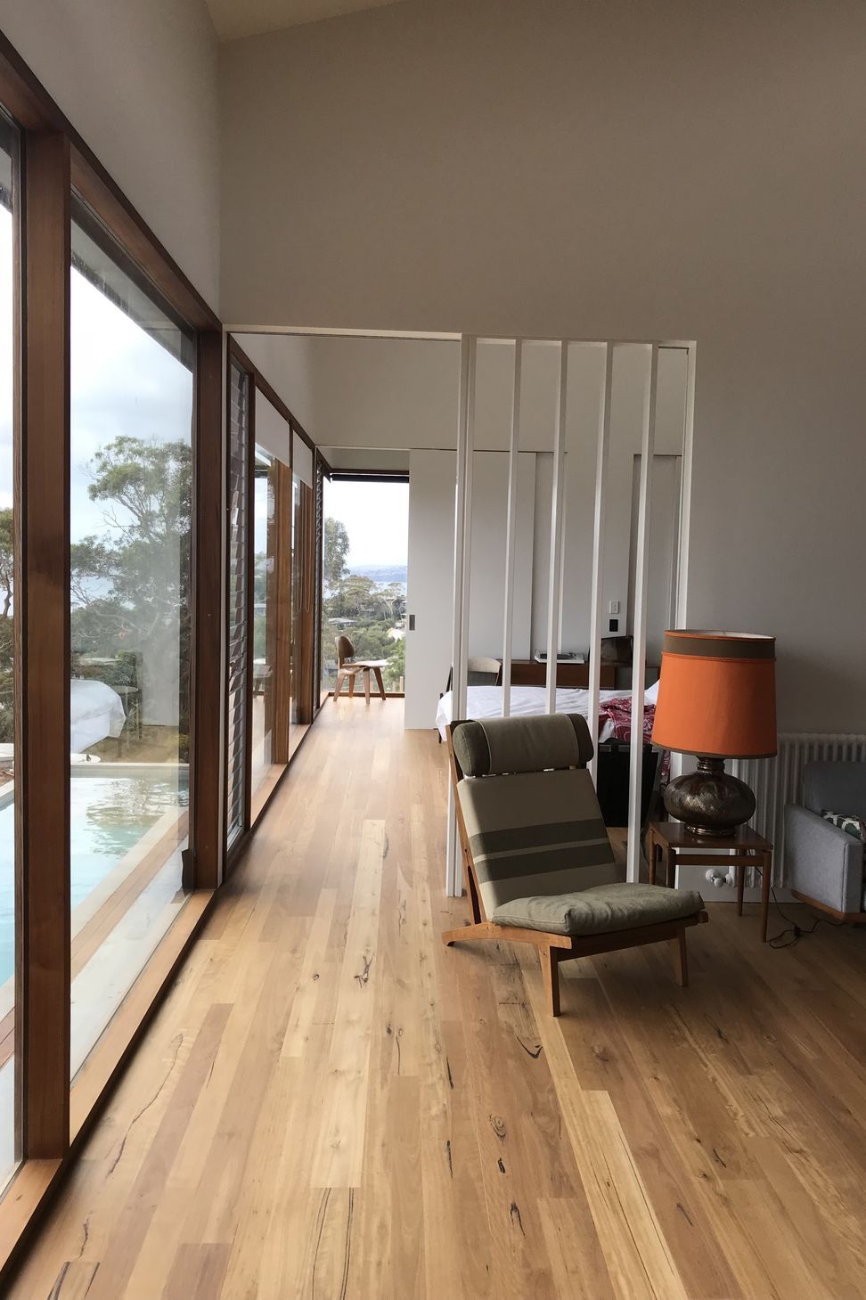 A minimalist vertical slatted screen maintains seamless hallway circulation, integrated with a secret door to close off the bedroom alongside timber-framed glass walls