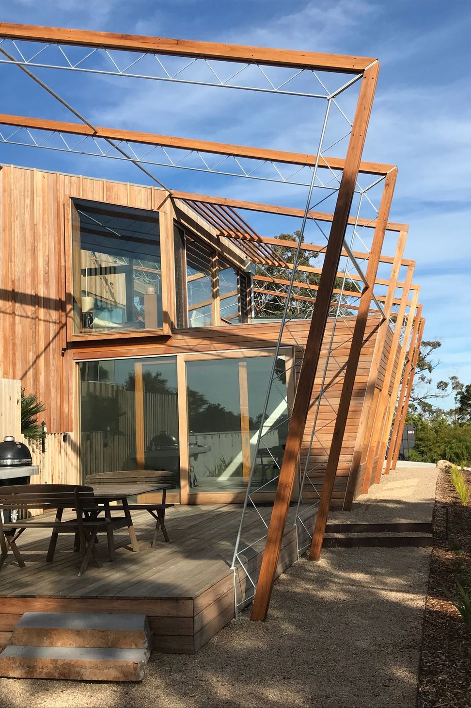 Angled timber trellis portals with steel rod bracing cast dynamic shadows across the tiered deck and glass window bays