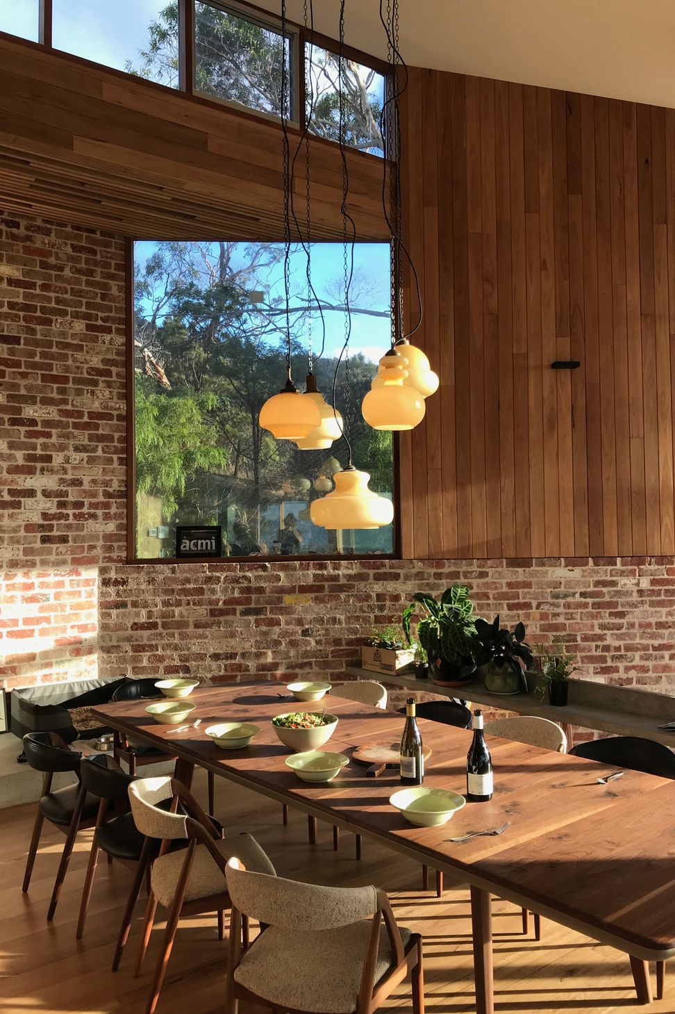 An organic cluster of Murano glass pendant lights illuminates the dining space, highlighting a recycled brick feature wall and vertical timber paneling
