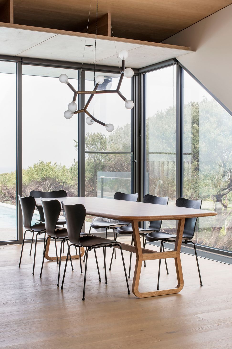 A feature brass and glass pendant suspended within the glass-walled dining space
