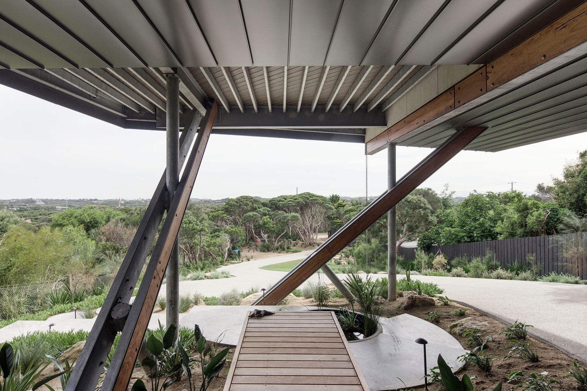 The intricate crossed structural legs of the upper level frame a welcoming entry timber boardwalk
