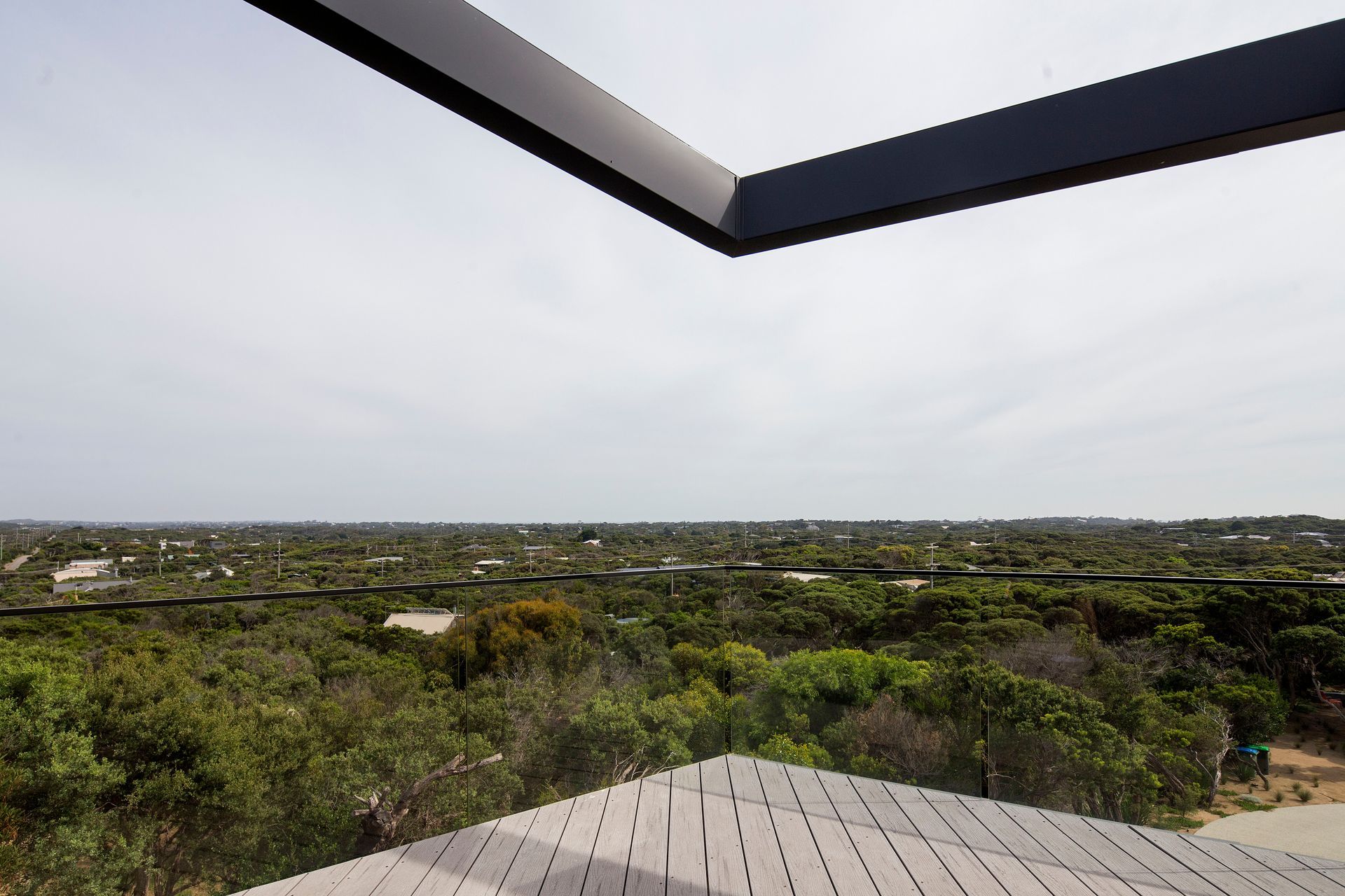 A hovering aluminum clad pergola beam frames the horizon line above the elevated timber deck