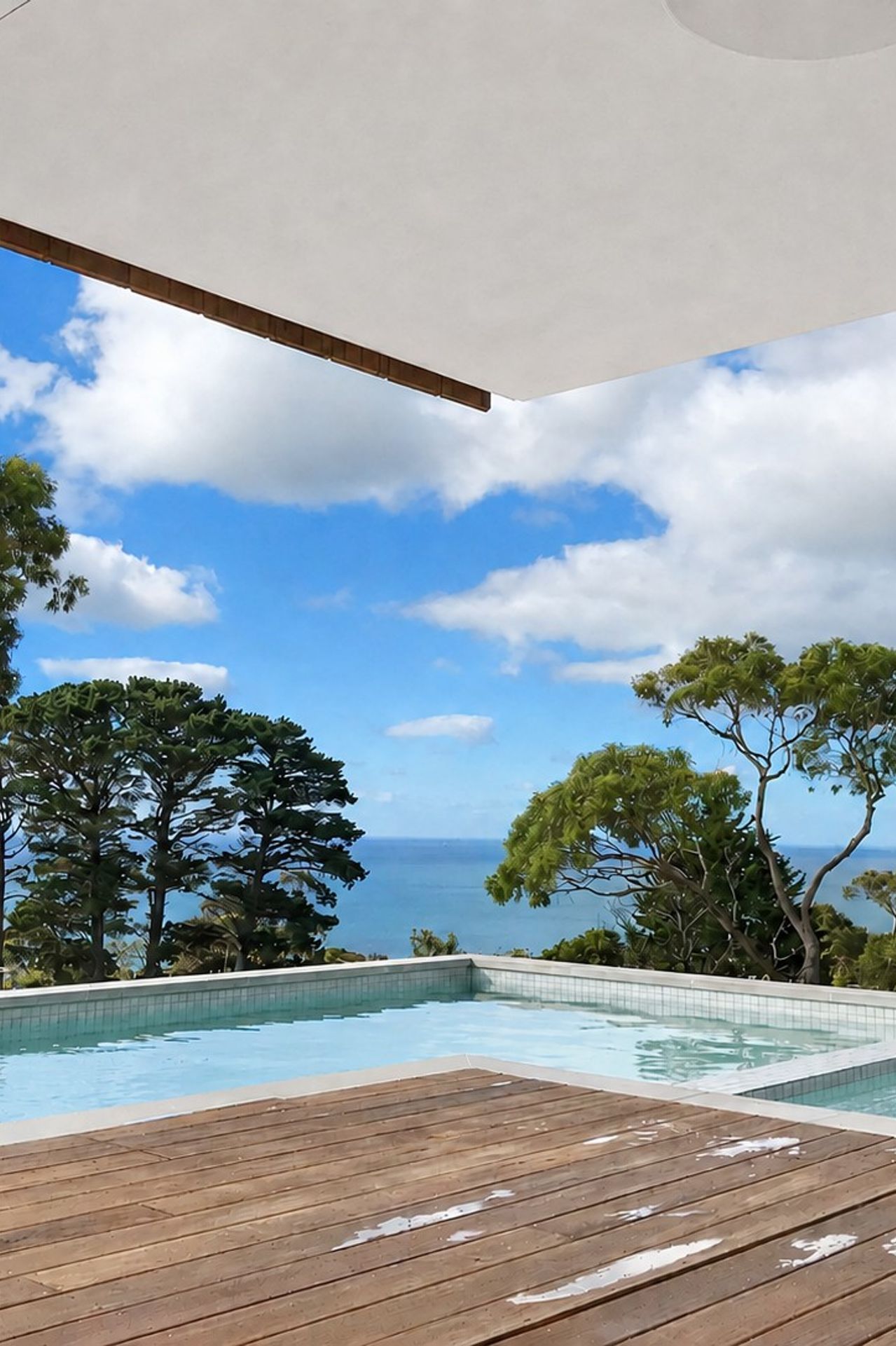 A white-tiled swimming pool and timber entertaining deck look out to sweeping ocean views, framed by a crisp cantilevered roof overhang