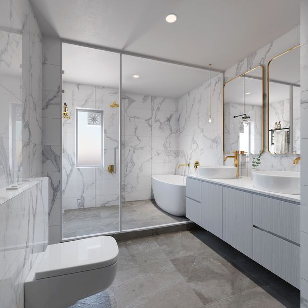 A bright, contemporary bathroom with full-height white marble-look wall tiles, large grey stone-look floor tiles, a frameless glass shower enclosure, freestanding white bathtub, wall-hung toilet, and a long pale grey floating vanity with double white vessel basins. Brushed gold fixtures, shower hardware, mirror frames, and pendant details provide refined accents.