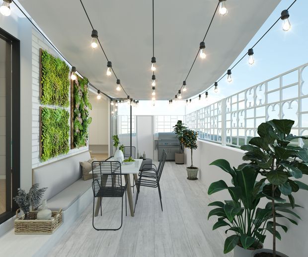 Bright enclosed terrace or sunroom with pale timber-look flooring, white walls, extensive glazing, decorative white breeze-block screening, hanging string lights, indoor plants, vertical living-wall panels, and a compact outdoor-style dining setting.