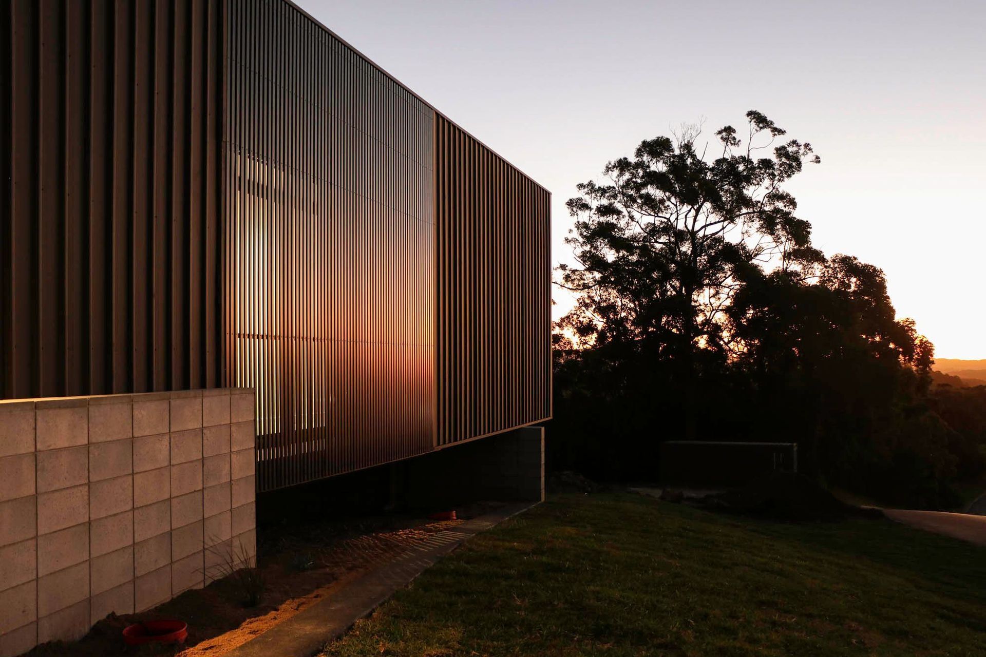 Seabrook and Borg Residence - Exterior. Dark cladding glowing at sunset among the trees.
