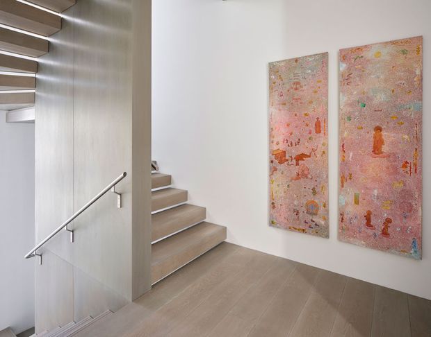 A bright, minimalist stairway and landing with broad light timber steps and matching timber flooring. A slim metal handrail runs along a pale vertical wall, while two colourful pink-toned artworks are mounted on the white wall beside the stairs. The space has clean lines, restrained detailing, and a calm contemporary appearance.
