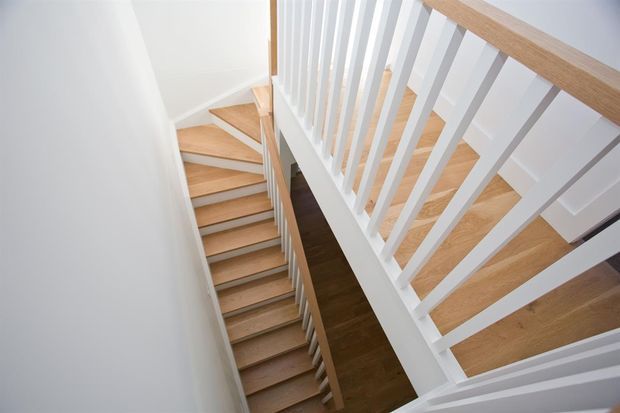 A bright, modern stairway viewed from above, featuring warm timber stair treads and handrails, white painted balusters and walls, and a compact multi-level stairwell.