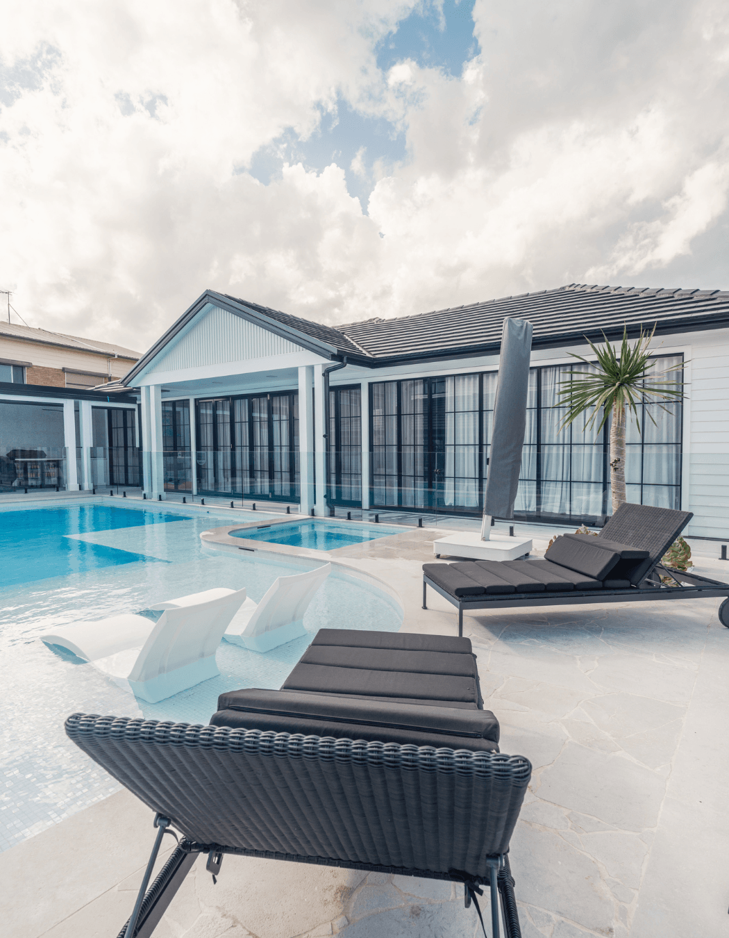 Glass walls open the living spaces to the pool, with Luna Chiaro Limestone flowing seamlessly from indoor to outdoor. The stone's neutral palette and Alfresco finish create a calm, cohesive backdrop for relaxed coastal living.