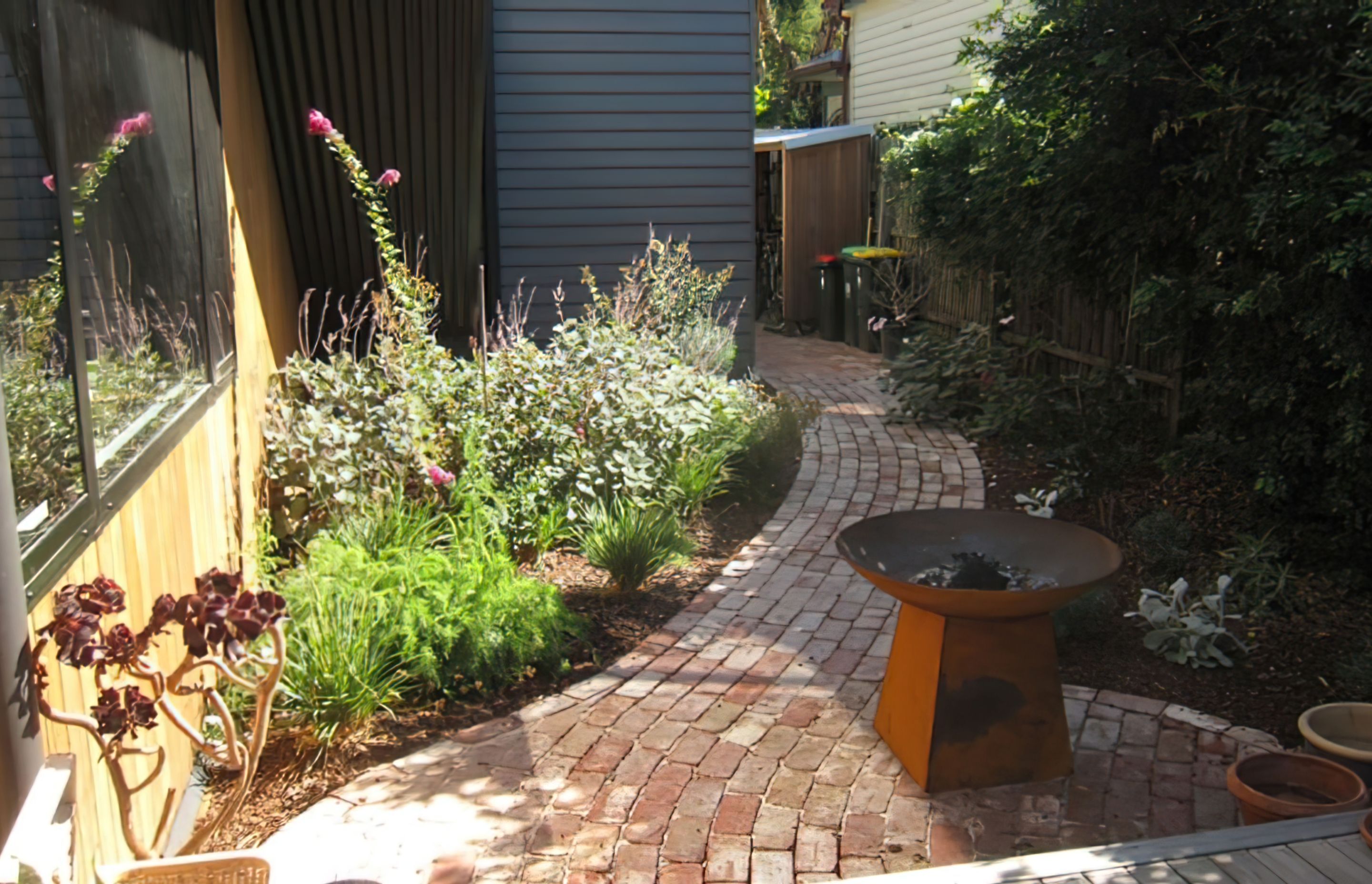 AFTER the garden design. A sinuous red brick path enters the deck at a small gathering node where a firepit is placed