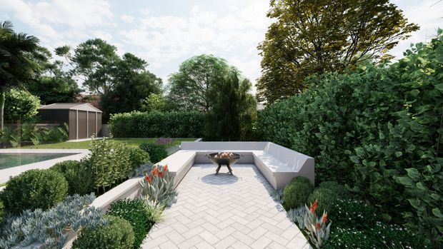 A landscaped outdoor terrace or courtyard with pale herringbone paving, built-in white rendered seating, a central fire bowl, and dense layered planting. The terrace overlooks a garden and swimming pool, with a small contemporary garden structure visible in the background.