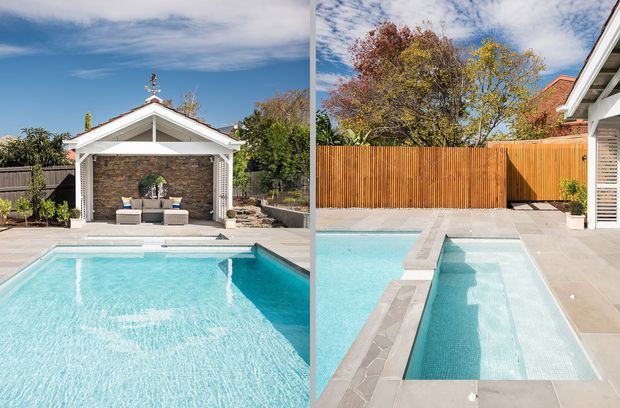 A bright outdoor residential pool area shown in a split view. The image features a large turquoise swimming pool, a narrow adjacent plunge pool or spa, pale paved surrounds, a timber privacy fence, and a small gabled pool pavilion with a stone-clad feature wall and seating. Mature trees and blue sky are visible in the background.