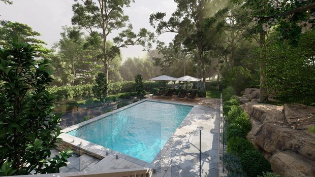 A landscaped outdoor swimming pool surrounded by dense mature greenery, clipped shrubs, natural rock retaining features, and pale stone paving. Poolside umbrellas and lounge seating sit at the far end, creating a secluded resort-like garden setting.