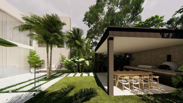 Rendered architectural view of a contemporary landscaped courtyard with a minimalist white building at left and a covered outdoor entertaining area at right. The pavilion has a flat roof, dark structural framing, a light soffit, stone feature wall, outdoor kitchen with a dome-shaped oven or barbecue, and a timber dining table with chairs. Tropical planting, lawn, stepping stones, and linear garden beds define the courtyard.