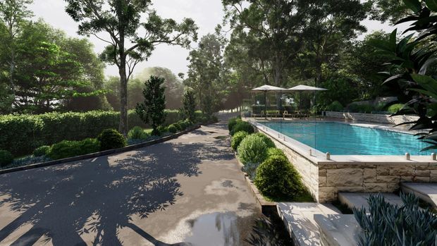 A landscaped outdoor pool area beside a paved garden walkway. The rectangular swimming pool has a raised natural-stone-clad edge, paved coping, and a small shallow step area, with manicured hedges, rounded shrubs, mature trees, and outdoor umbrellas surrounding the space.