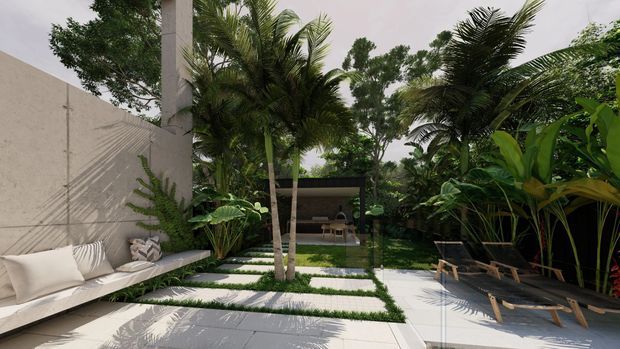 A lush tropical courtyard or outdoor living area with a minimalist paved patio, pale concrete privacy walls, built-in cushioned seating, tropical palms and broad-leaf planting. A shaded open pavilion or lounge structure sits at the rear, while timber loungers occupy the right side. The scene has a refined resort-like atmosphere with strong indoor-outdoor continuity.