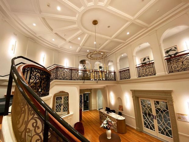 Grand multi-level residential foyer with a sweeping curved staircase, ornate wrought-iron balustrades, arched openings, decorative paneled coffered ceiling, chandelier, warm timber flooring, and traditional embellished doors and trim.