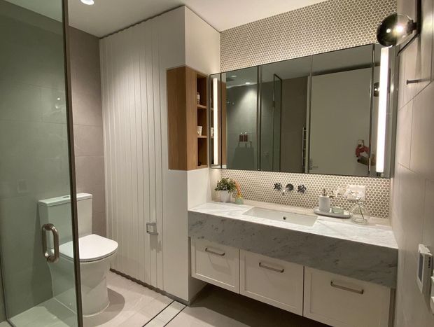 Contemporary bathroom with a floating double vanity, white marble-look benchtop, large mirrored wall cabinet, tiled shower enclosure, wall-hung storage, and a separate toilet area. The room uses light neutral finishes with a patterned mosaic tile backsplash and warm timber joinery accents.
