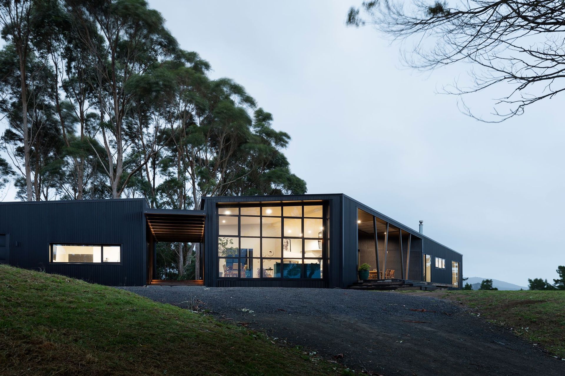 Located on a semi-rural, two-acre block on the west coast of the North Island, this home sits atop a ridgeline and revels in its backdrop of mature eucalypts and an outlook that takes in the west coast mountain ranges and distant ocean view.